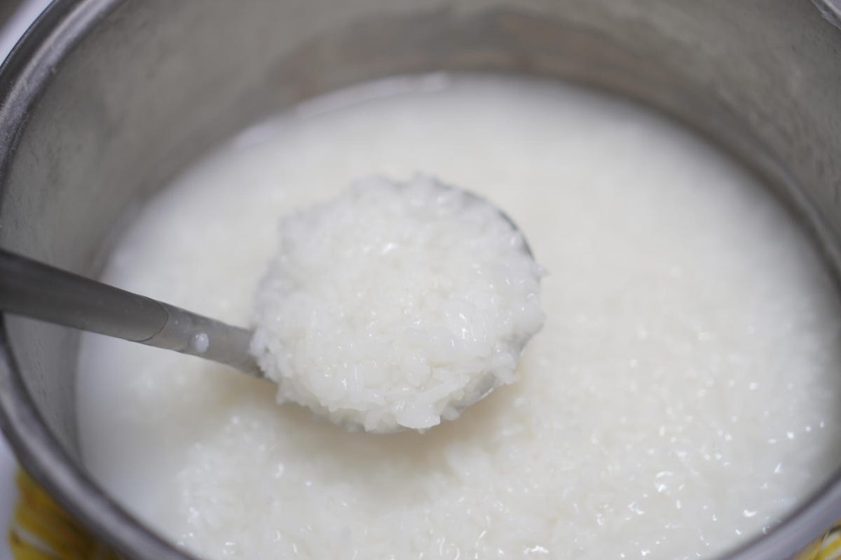 A ladle scoops up white rice cooked in a silver pot.